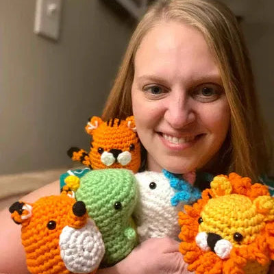 Woman holding four colorful crocheted animal toys in a home setting.