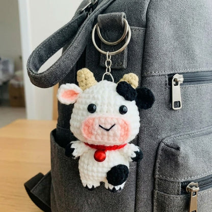 Crochet cow keychain by WoolyArtis featuring a kawaii amigurumi farm animal plush, perfect as a cute bag charm or purse pendant.